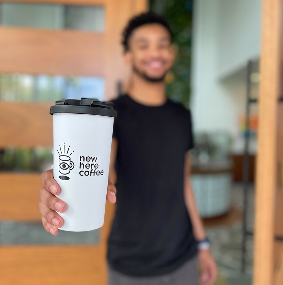 A man holding a cup of New Here Coffee